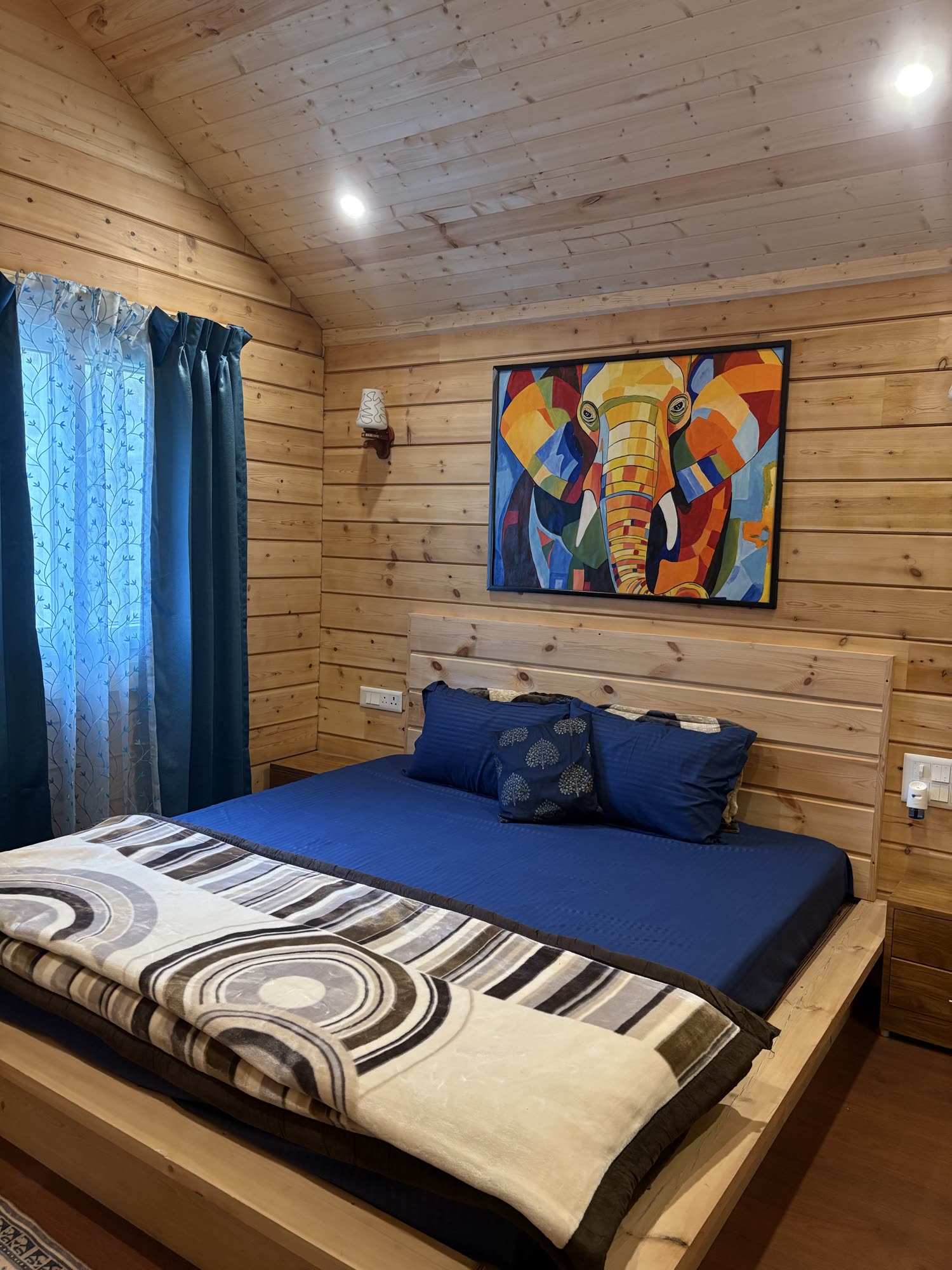 Master bedroom with a king-size pine wood bed and a vibrant elephant painting